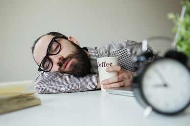 A Man Holding A Cup Of Coffee Sleeping On The Desk